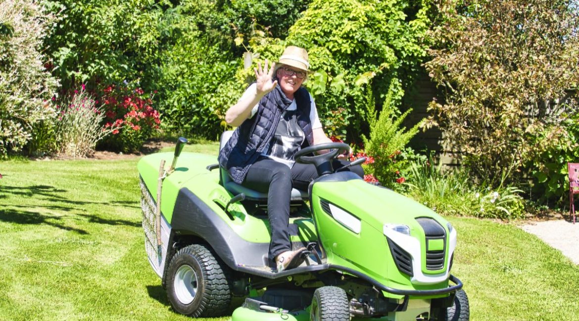 ride-on-mower-mature-woman-driving-a-tractor-lawn-mower-in-garden-with-flowers-min