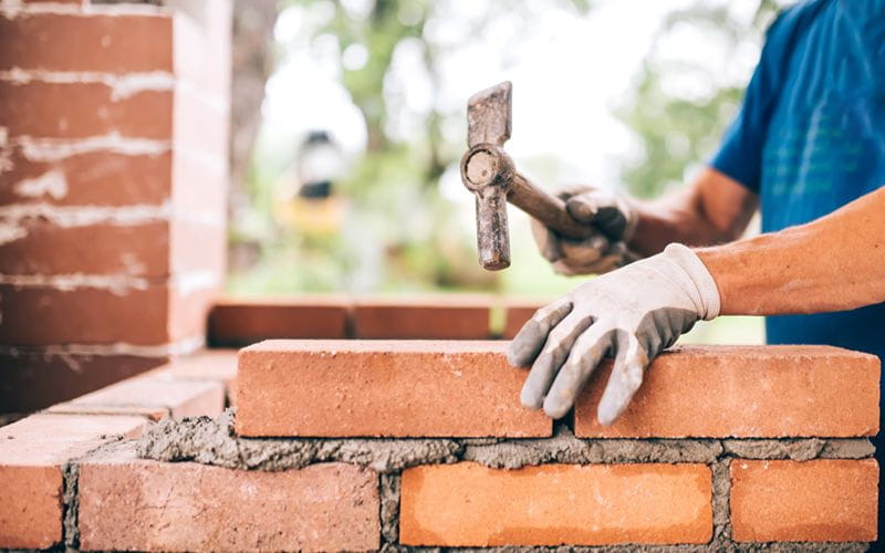 concrete-mixer-worker-building-exterior-walls-using-hammer-for-laying-bricks-in-cement-detail-of-worker-with-tools (1)